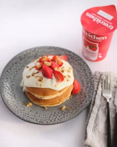 Pancakes with strawberry yoghurt and strawberries next to a tub of clotted cream yoghurt